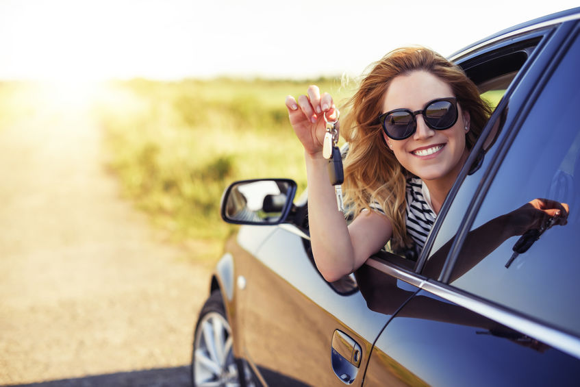 Lady leaning out window of her new car, dangling her keys and smiling